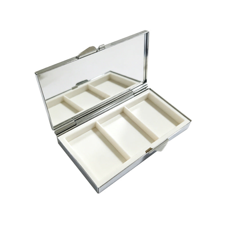 Open metal pill box showing the mirror in the lid and three empty compartments