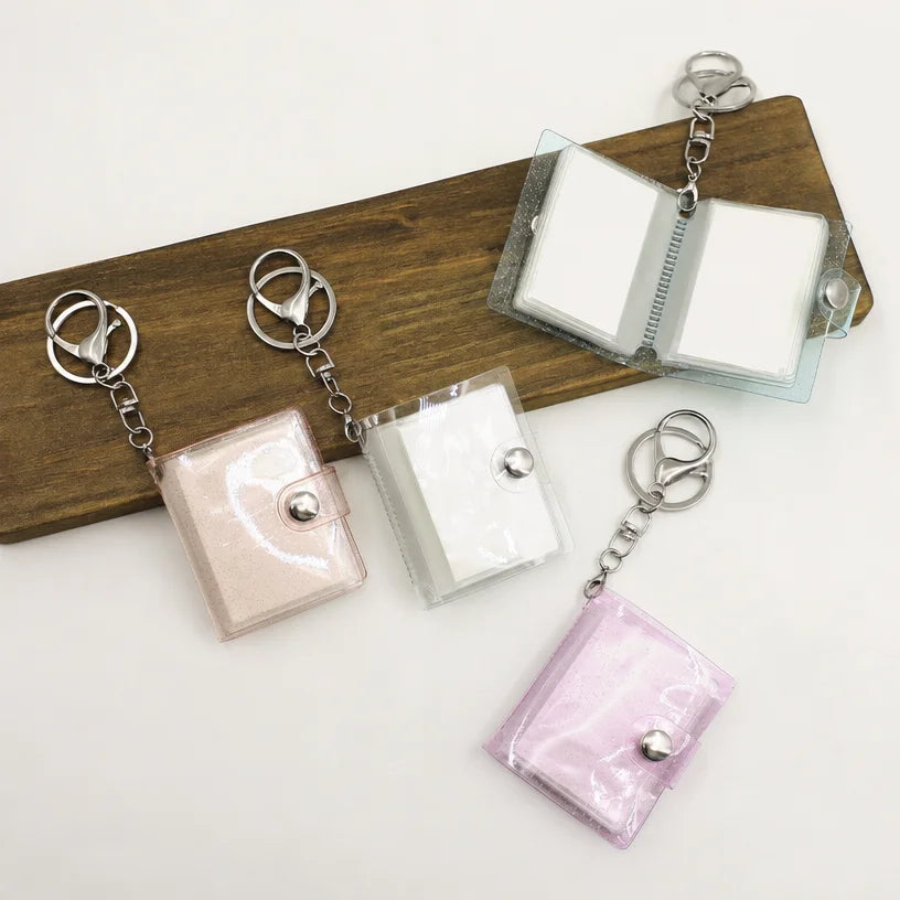 Blank mini photo album keychains on a wooden board, one opened to show the inner pages