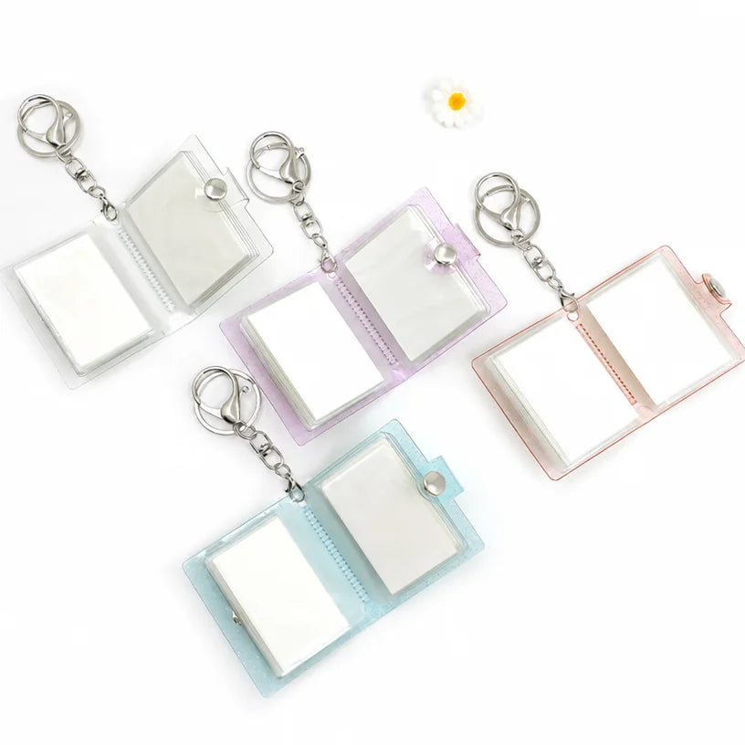 Four blank photo album keychains opened flat, showing the hinged white sleeves