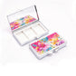 Two blank chrome metal pill boxes, one open showing three compartments and one closed with a printed floral design