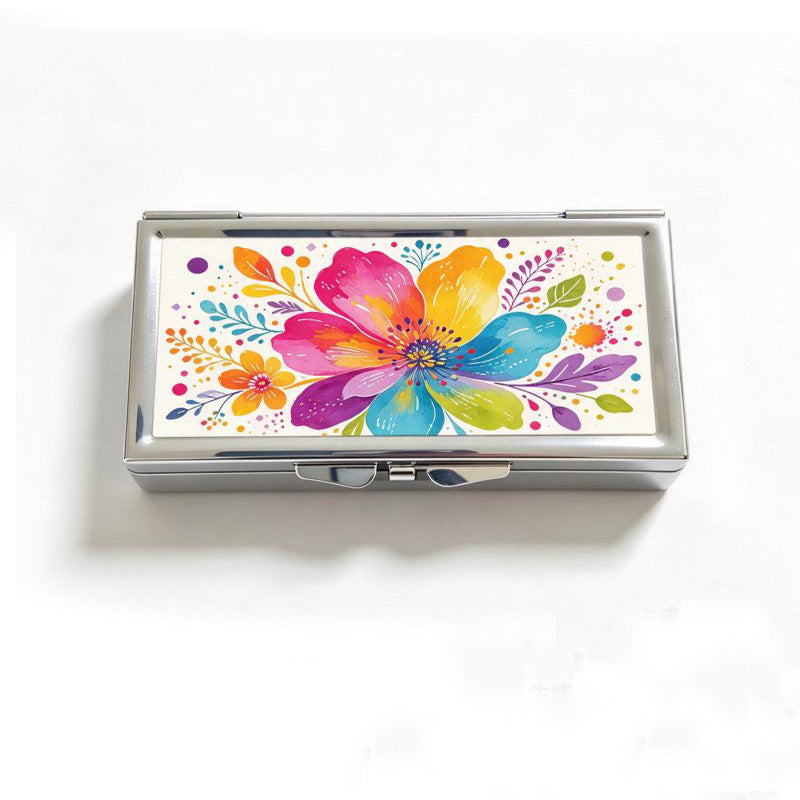 Closed chrome pill box lid with a pressed colourful floral design